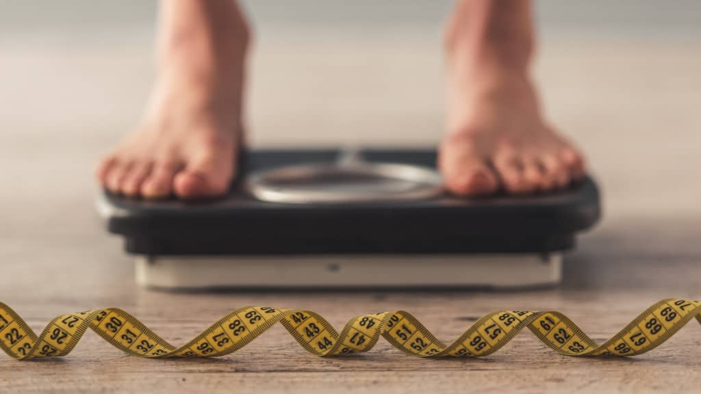 feet on a scale with measuring tape - weight loss